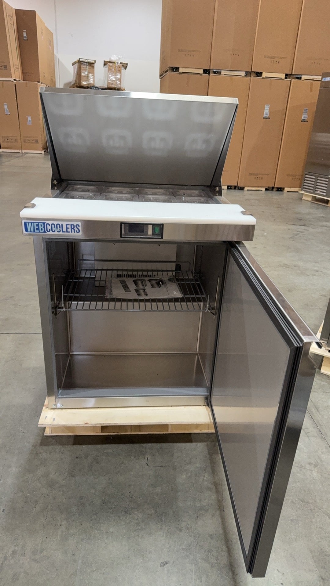 Stainless steel refrigerator on a pallet with cardboard boxes in the background