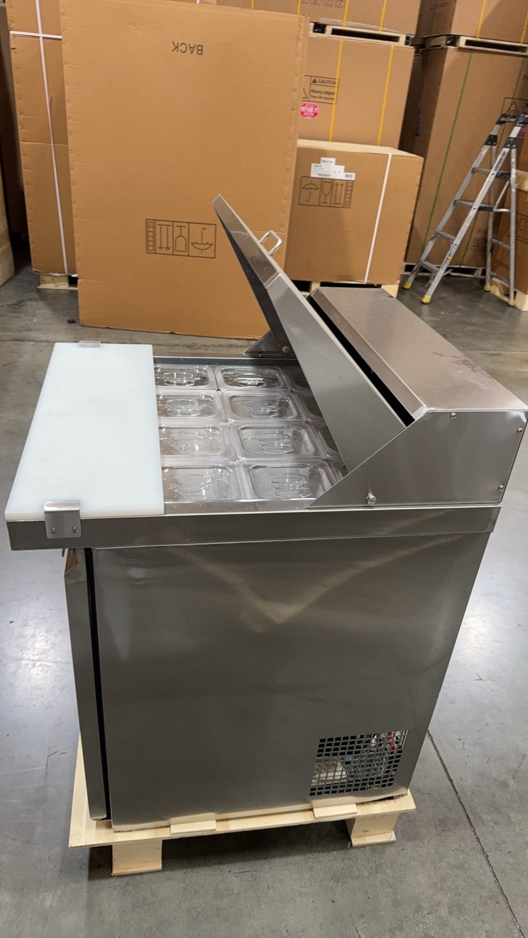 Stainless steel refrigerator on a pallet with cardboard boxes in the background