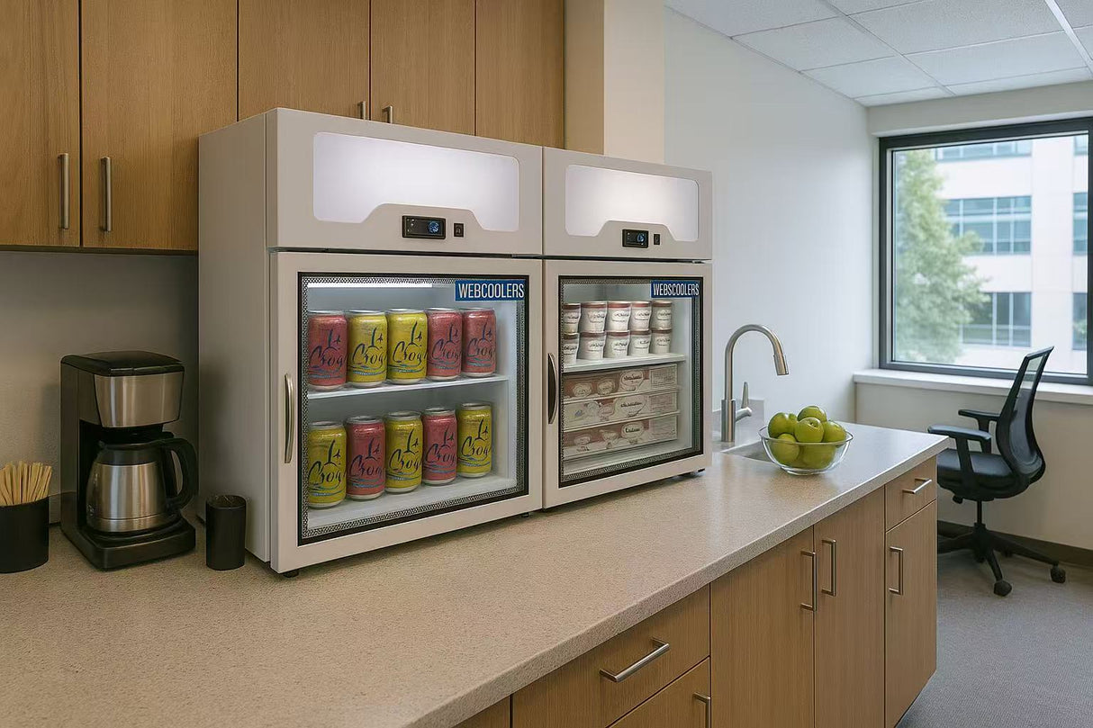Modern kitchenette with refrigerator, coffee maker, and fruit bowl in an office setting.
