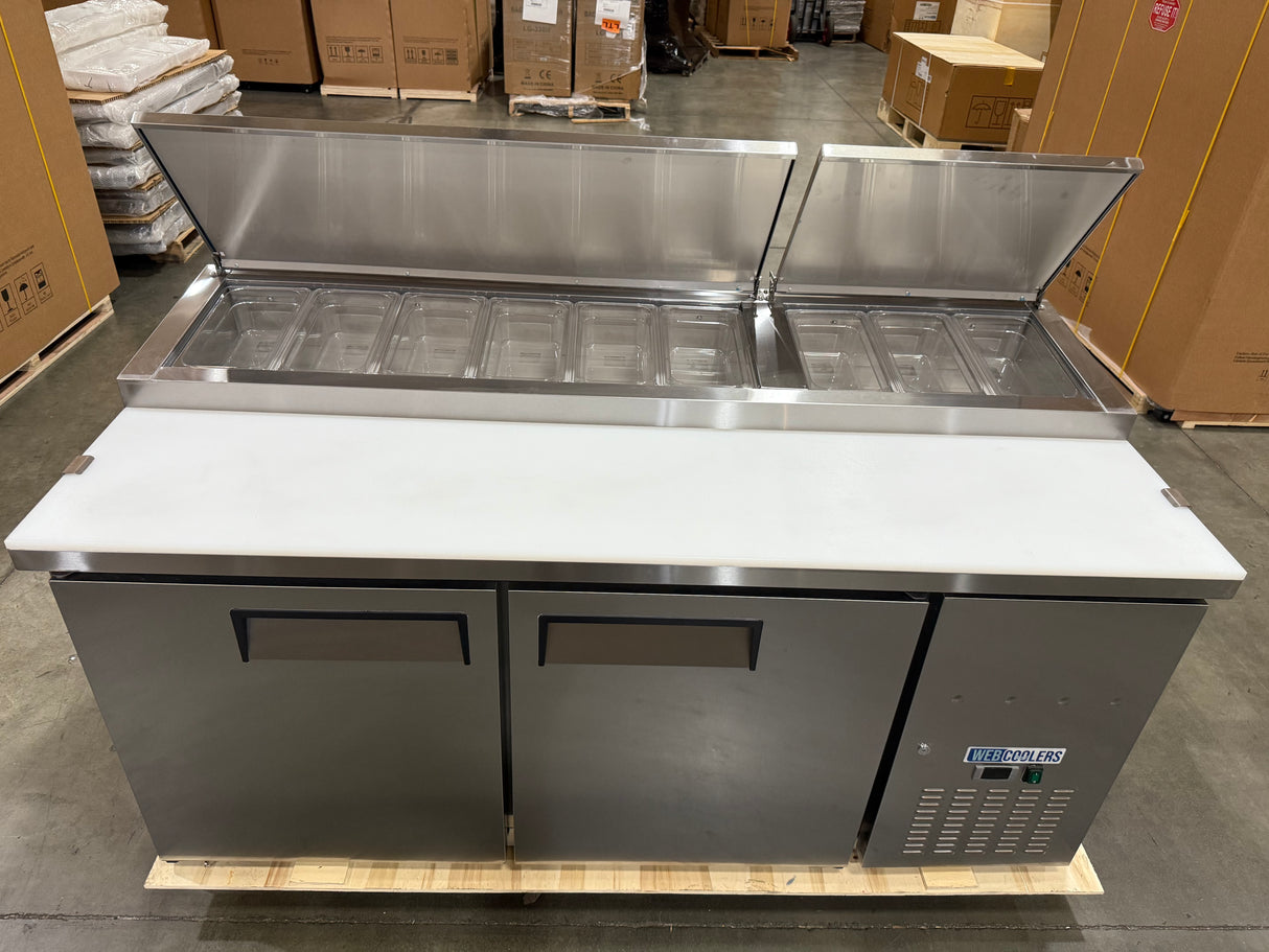 Stainless steel refrigerated counter with open doors in a warehouse setting