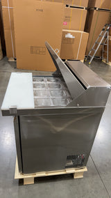 Stainless steel refrigerator on a pallet with cardboard boxes in the background