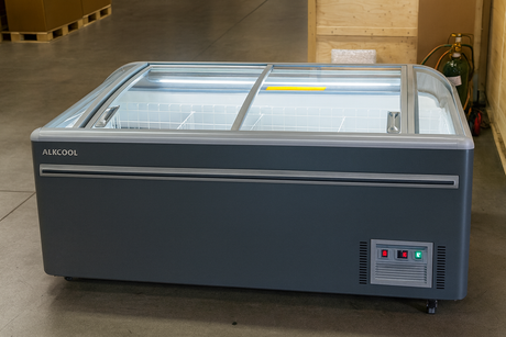 Large freezer with glass lid on a concrete floor, brand 'ALKCOOL' visible