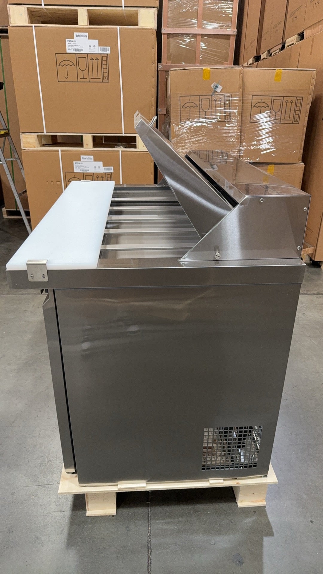 Stainless steel oven on a pallet in a warehouse setting with cardboard boxes in the background.