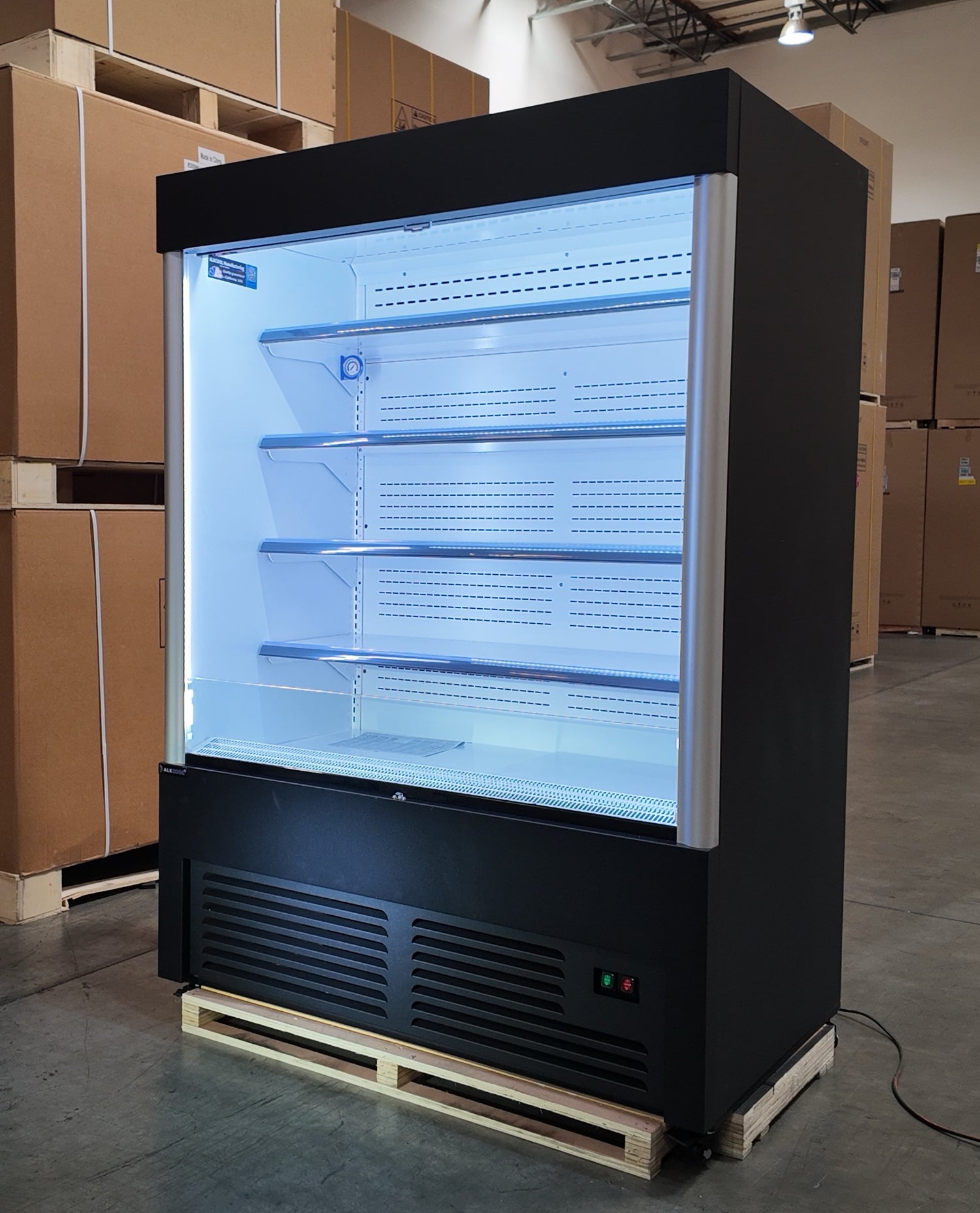 Large black refrigerated display case in a warehouse setting with cardboard boxes.