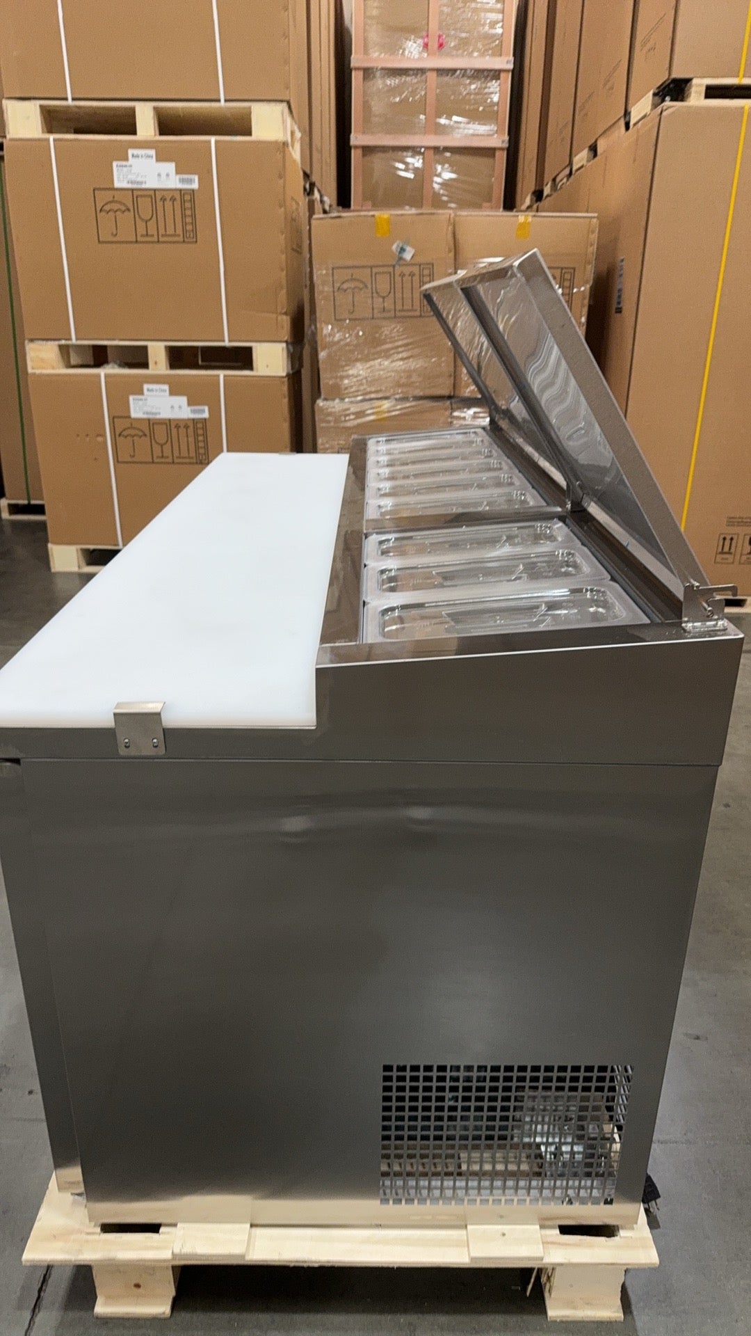 Stainless steel freezer on a wooden pallet with cardboard boxes in the background