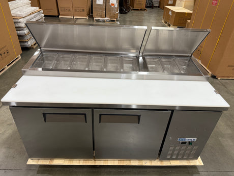 Stainless steel refrigerated counter with open doors in a warehouse setting